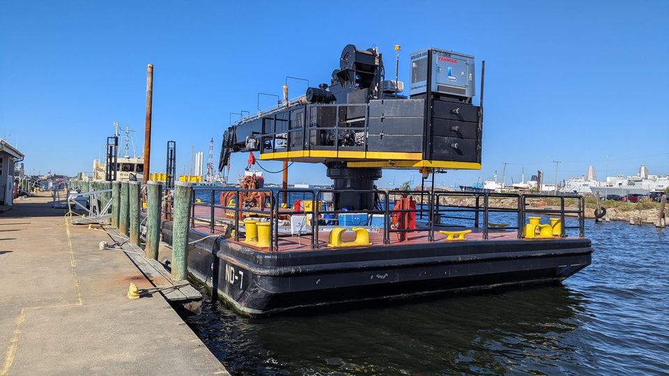 Crane barge with a knuckle-boom crane moored at a pier in a harbor